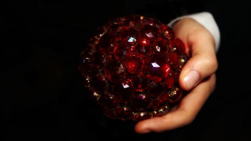 Close-up of hand holding strawberry over black background