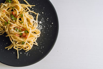 Close up spaghetti pasta sprinkled with cheese parmesan and green onions on a black plate