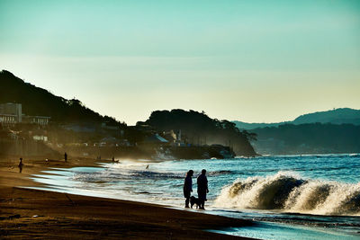 Silhouette people standing on beach against sky in the morning