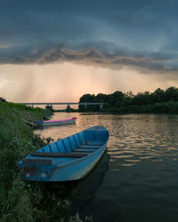 Boat moored on lake against sky during sunset