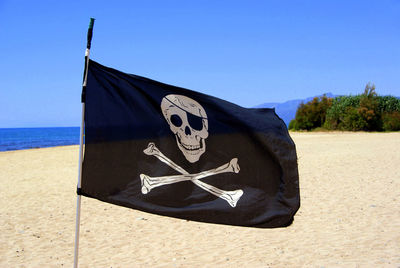 Close-up of pirate flag at beach against sky