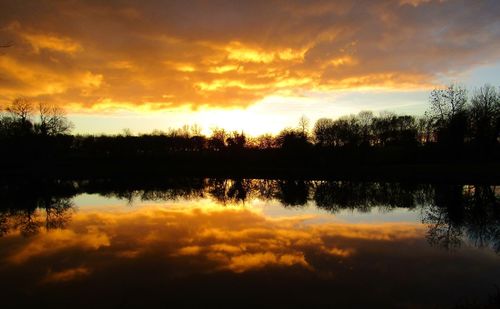 Reflection of silhouette trees on water against orange sky