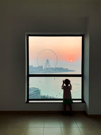 Little boy silhouette looking outside at scenic marine view with dubai eye at sunset