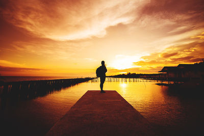 Rear view of silhouette man standing on sea against sky during sunset