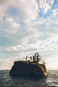 Men standing on cliff by sea against sky