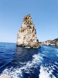 Rock formation in sea against clear blue sky