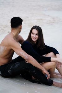 Portrait of young couple sitting at beach looking away