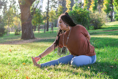 Beautiful young woman with long african braids is doing yoga outside in a park.