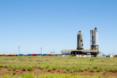 Factory on field against clear blue sky