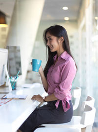 Businesswoman holding coffee cup while sitting in office