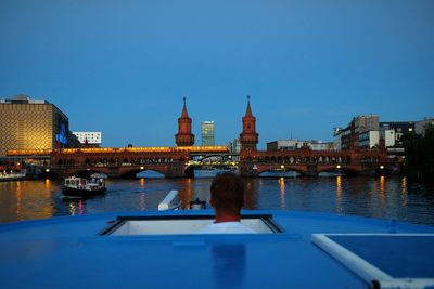 Rear view of man in boat by oberbaum bridge over river spree against clear sky at dusk
