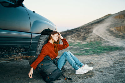 Young woman looking away while sitting in car against sky