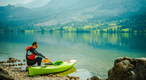 Man sitting by kayak at lakeshore