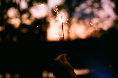 Cropped hand of person holding illuminated sparkler at dusk
