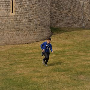 Full length of boy running on grassy field against old fort