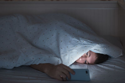 Tired man lying in bed under the blanket using smartphone at late night, can not sleep. insomnia