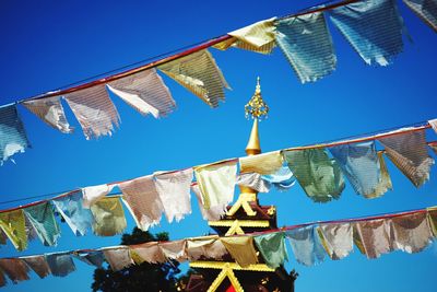 Low angle view of flags hanging outside building against blue sky