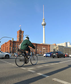 Man riding bicycle on street amidst buildings in city against sky