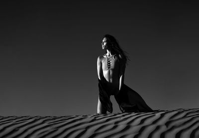Low angle view of woman looking away on sand against sky