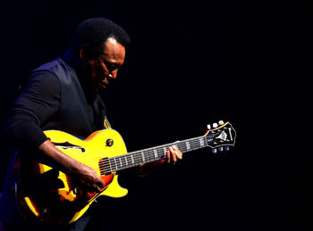 Man playing guitar against black background