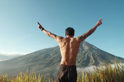Rear view of shirtless man standing against mountain