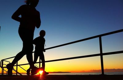 Silhouette friends jogging on beach at sunrise