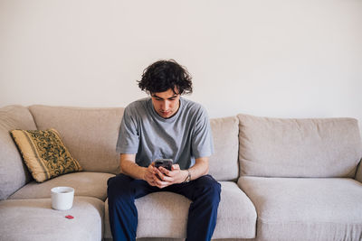Man using mobile phone while sitting by coffee cup on sofa