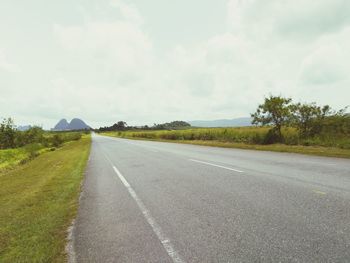 Empty road amidst field against sky