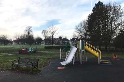 Empty park bench on field against sky