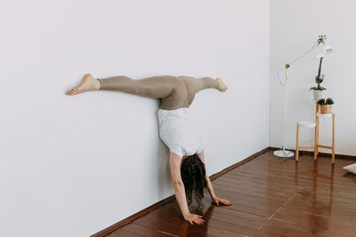 Full length of man skateboarding on hardwood floor against wall