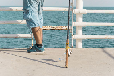 Low section of man standing on railing by sea