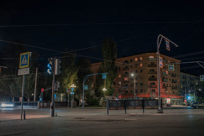 Illuminated street by building against sky at night