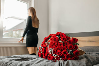 A huge beautiful bouquet of scarlet roses on a bed in a bedroom or hotel and a beautiful girl 