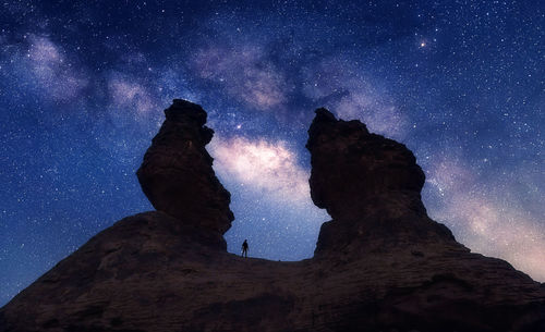 Low angle view of silhouette man on rock formation against star field at night