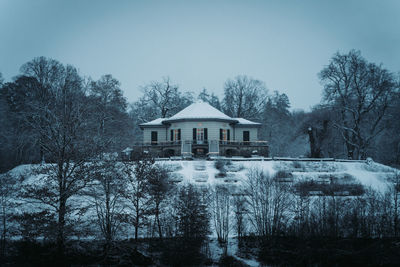 Houses and trees by building against sky during winter