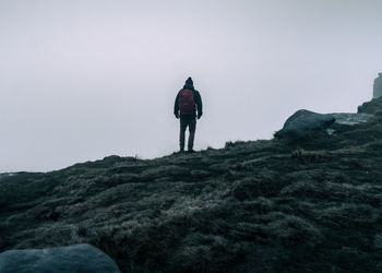 Lone man standing on edge of mountain cliff looking out into mist