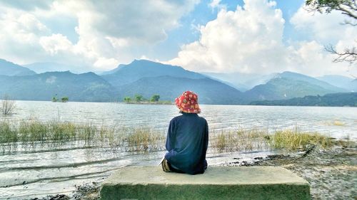 Rear view of woman sitting by lake against mountains