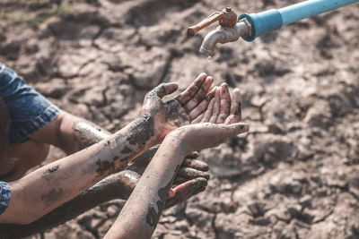 Cropped dirty hands below faucet on barren land during drought