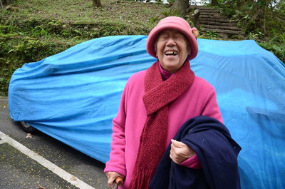 Cheerful senior woman standing against car with blue covering at parking lot