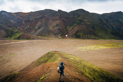 Hiker photographing lake and mountains against cloudy sky