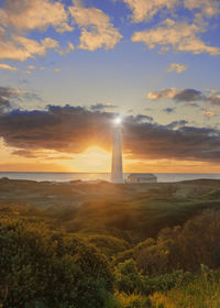 Lighthouse by sea against sky during sunset
