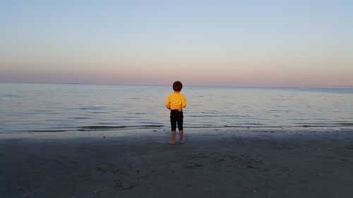 Rear view of man standing on beach against sky during sunset