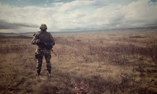 Full length of army soldier standing on field against cloudy sky