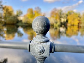 Close-up of metal railing by lake against sky