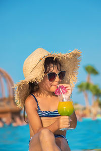 Portrait of young woman drinking water against clear blue sky