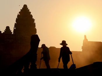 Silhouette people by historic building against sky during sunset