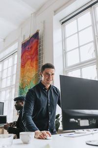 Smiling young businessman using desktop pc at desk in office