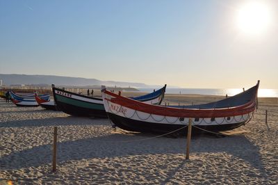 Boats moored on beach against sky during sunset