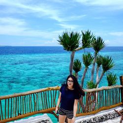 Portrait of young woman standing on palm tree against sea