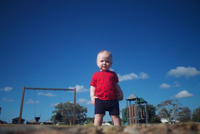 Portrait of boy standing on land against blue sky